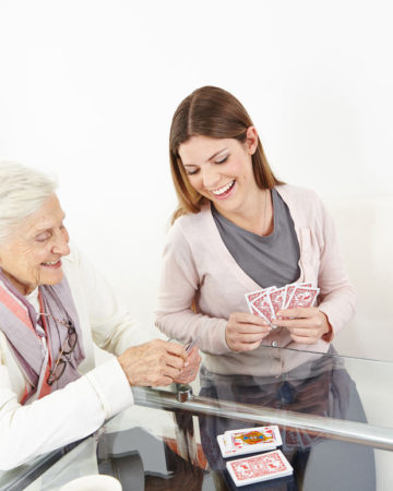 25216493 - happy senior woman playing cards with smiling granddaughter at home